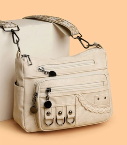 Detail of cream canvas crossbody bag featuring multi-pocket zippers and ethnic strap