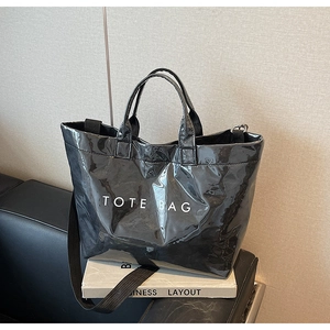 Close-up of a glossy black tote bag with white TOTE BAG text and long shoulder strap