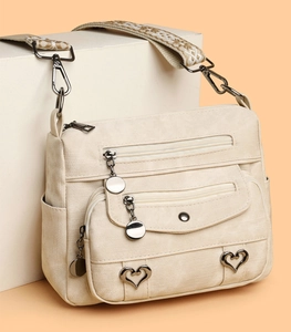 Close-up of cream crossbody bag featuring multiple zipper pockets and heart metal buckle