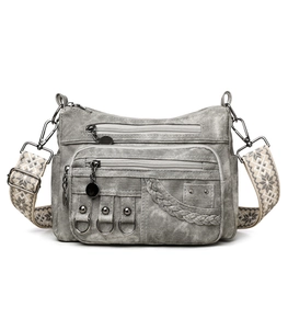 Detail view of grey canvas crossbody bag showing metal rings, studs and woven strap texture