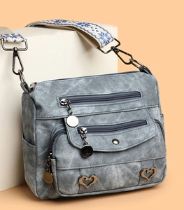 Detail of multi-pocket crossbody bag with heart charms and woven shoulder strap