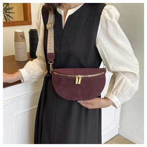 Detail of burgundy suede half-moon chest bag with wide embroidered strap and gold zippers