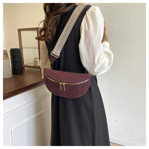 Detail of wine red crossbody bag with textured fabric, wavy strap and gold zippers