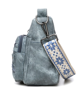 Detail of light blue denim crossbody bag featuring an embroidered wide snowflake strap