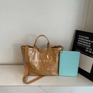 Large camel tote bag with glossy wrinkled texture and shoulder strap next to a tablet