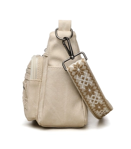 Detail of beige canvas crossbody bag featuring functional side zippers and ethnic strap