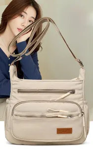 Close-up of beige waterproof crossbody bag showing multiple zippers and leather brand tag