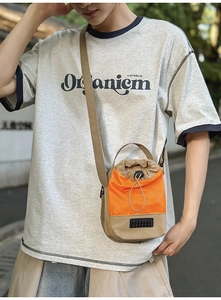 Outdoor shot of small khaki and orange drawstring bucket bag with adjustable strap