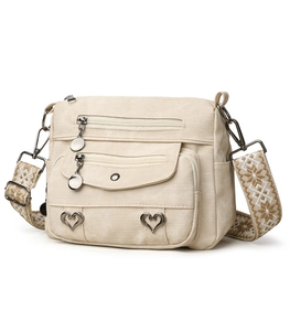 Close-up of cream crossbody bag with multiple zippers and ethnic pattern woven strap