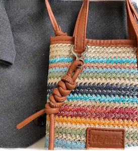 Detail of colorful woven straw tote with brown leather handles and decorative knot