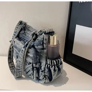 Détail du sac bandoulière en denim bleu avec poche latérale élastique pour bouteille d'eau