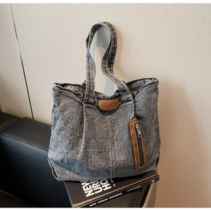 Détails d'un sac cabas en denim délavé avec patch en cuir brun et poche zippée pratique