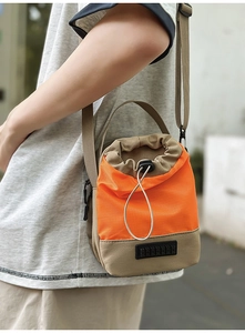 Detail of a bright orange and khaki drawstring crossbody bag with durable nylon material