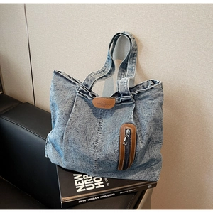 Détail du sac cabas en denim délavé vintage avec logo en cuir marron et poche zippée