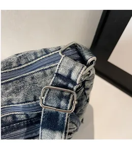 Détail de la boucle en métal et des coutures sur un sac bandoulière en jean délavé