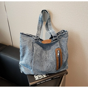 Gros plan sur le sac cabas en denim délavé avec poche en cuir et patch de la marque