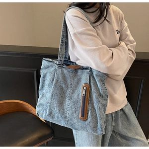 Détail du sac cabas en denim délavé avec patch en cuir marron et fermeture éclair verticale