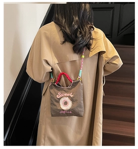 Détail du sac en toile brodé avec poignées rondes rouges et bandoulière tissée colorée