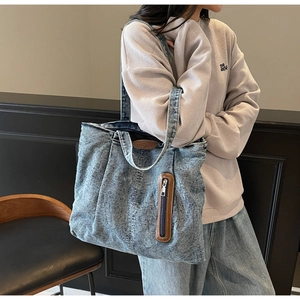 Détail de la texture denim délavé et de l'écusson en cuir sur le grand sac fourre-tout