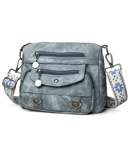 Detail of light blue denim crossbody bag featuring heart buckles and ethnic embroidery