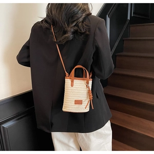 Detail of straw bucket bag with brown leather trim and shoulder strap on model