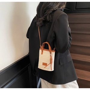 Detail of hand-woven straw bucket bag with brown leather strap and contrast texture