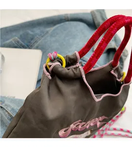 Détail du sac en tissu marron avec anses en corde rouge et broderie rose élégante
