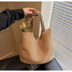 Detail of straw woven tote bag featuring smooth leather handles and rivet accents