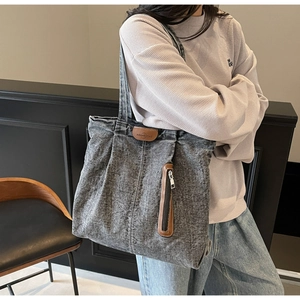 Détail du sac cabas en denim délavé montrant l'accent en cuir et la poche zippée