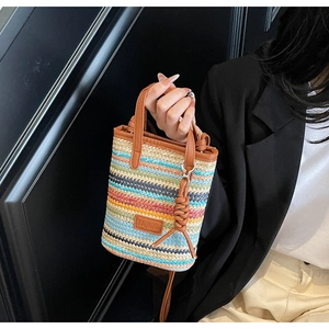 Close-up of a colorful woven straw mini bag with brown leather handles and a side knot detail
