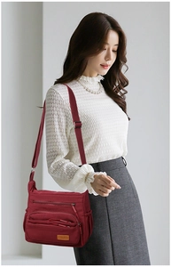 Close-up of burgundy nylon crossbody bag featuring multiple zipper compartments and side pockets