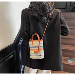 Crossbody view of a colorful striped straw bucket bag worn over a black blazer