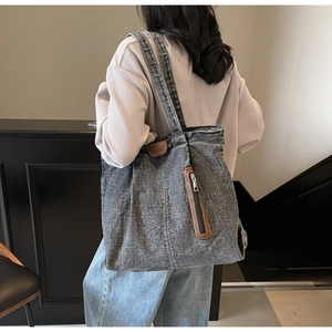 Détail du sac cabas en denim délavé gris avec garniture en cuir marron et poche zippée verticale
