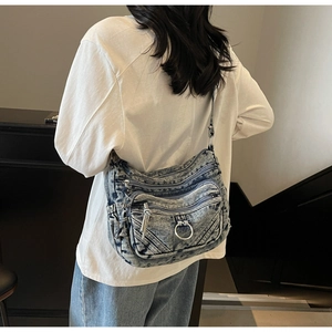 Détail du sac bandoulière en denim bleu avec poches zippées et anneaux métalliques