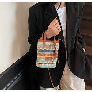 Detail view of mini hand-woven straw bag with colorful stripes and brown leather handle