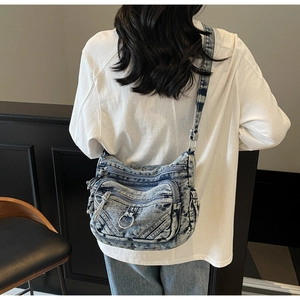 Sac bandoulière en denim bleu avec compartiments zippés et sangle réglable porté par un modèle
