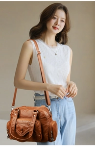 Close-up of brown faux leather shoulder bag with woven edge detail and multiple zippers