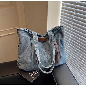 Détail du sac cabas en jean délavé bleu clair avec logo en cuir marron et poche zippée pratique