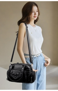 Detail of black soft leather crossbody bag featuring woven texture and floral zipper charms