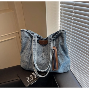 Détail du sac cabas en jean délavé bleu avec patch en cuir marron et poche zippée