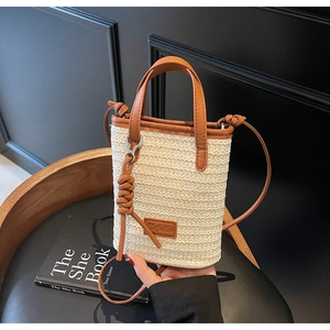 Close-up of woven straw bucket bag with brown leather trim and crossbody strap
