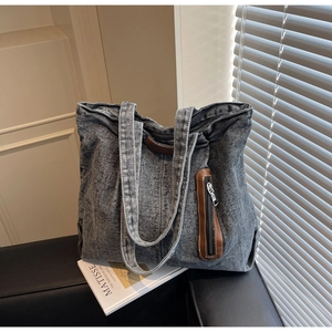 Détail du sac cabas vintage en denim délavé avec poche zippée en cuir sur canapé