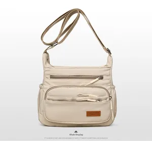 Detailed view of khaki crossbody bag featuring multiple zipper pockets and brand label