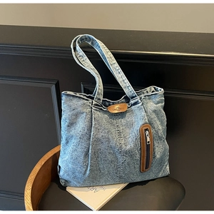 Détail du sac cabas vintage en denim délavé avec logo en cuir et poche zippée sur une chaise