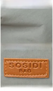 Detail of light gray woven canvas fabric and brown leather SOSIDI BAG logo patch