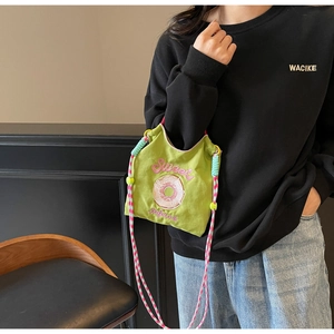 Détail du sac bandoulière en toile verte avec broderie donut et sangle tressée colorée