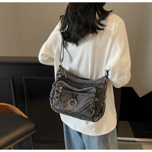 Détail du sac bandoulière en denim foncé avec plusieurs zips et boucle argentée