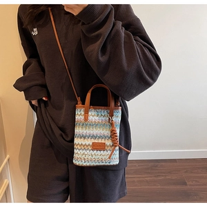 Detail of hand-woven straw crossbody bag with brown leather handles and logo plate