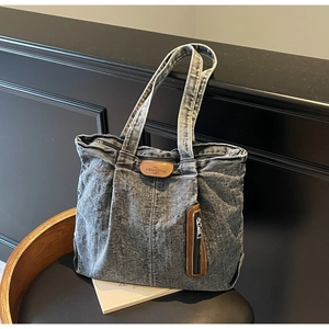 Détail du sac cabas en jean gris vintage avec zip latéral et patch en cuir sur une chaise