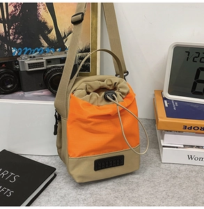 Detail of khaki and orange drawstring bucket bag with buckle and woven logo patch